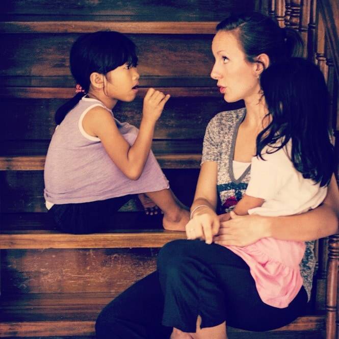 A young mother holds a little girl and sits by another little girl.