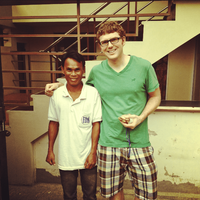Two men pose for a photo in front of stairs.