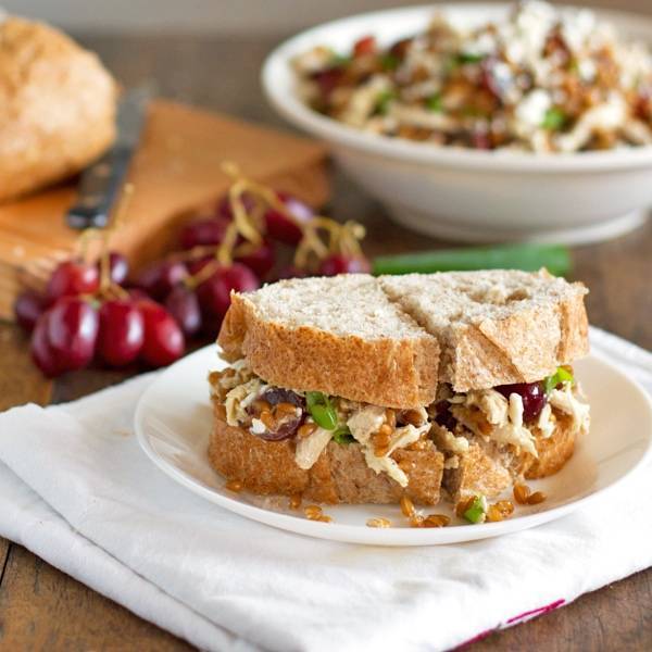 Sandwich filled with honey chicken salad with grapes and feta on a plate.