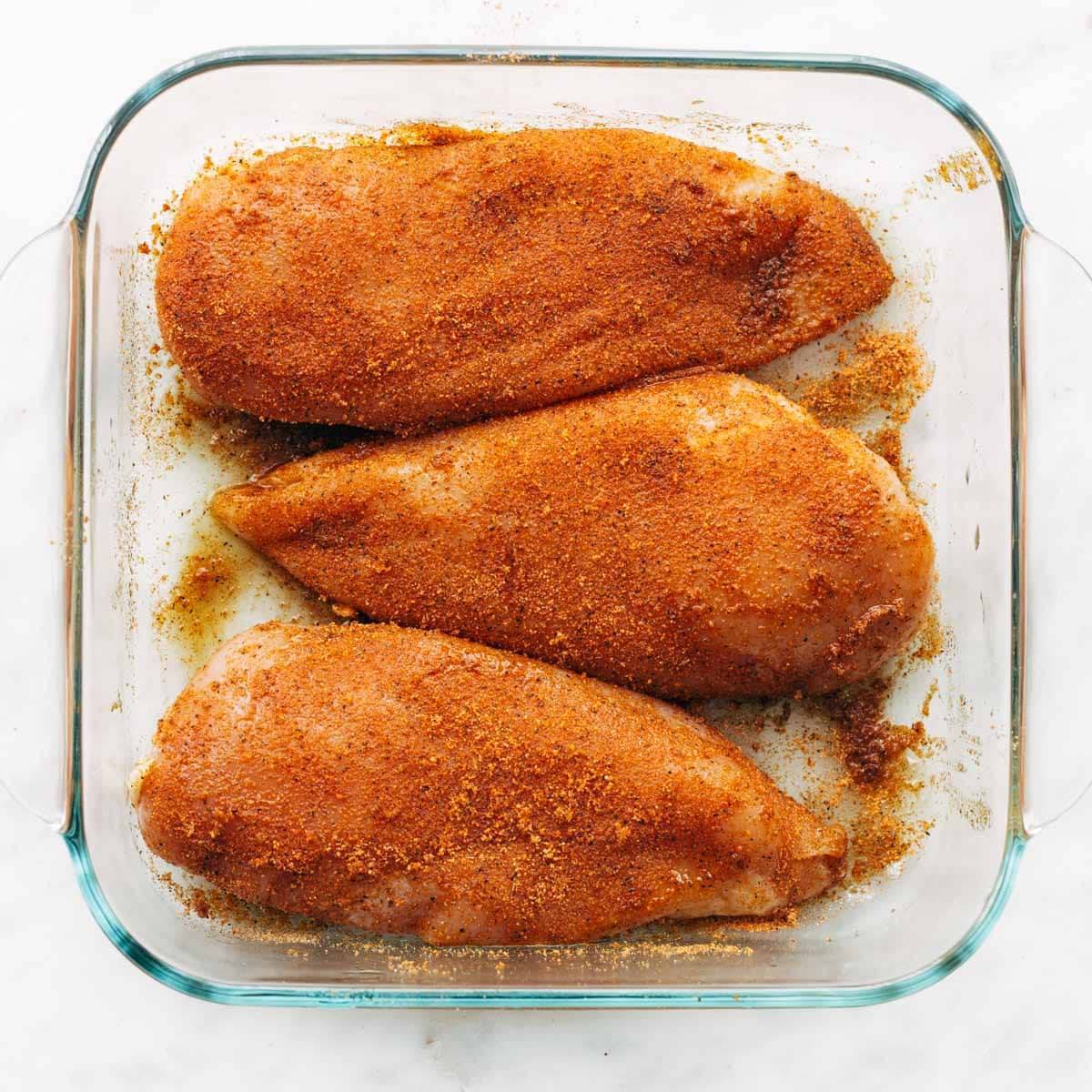 Seasoned chicken breasts in a pan.