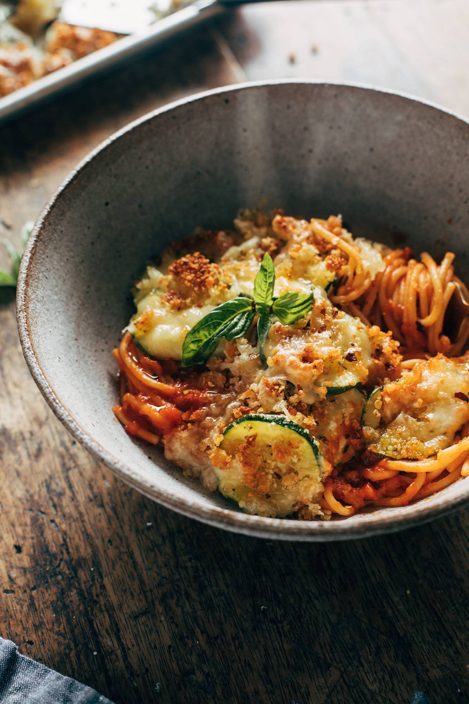 Spaghetti with crispy zucchini in a bowl with melted cheese and fresh basil on top.