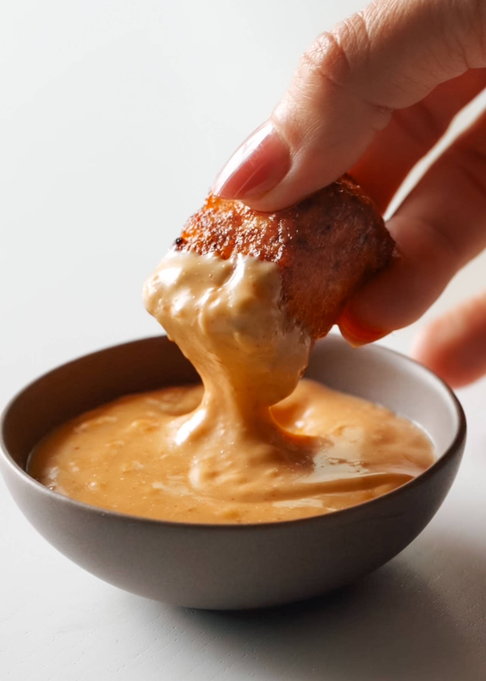 Dipping a piece of tofu into a bowl of gochujang sauce.