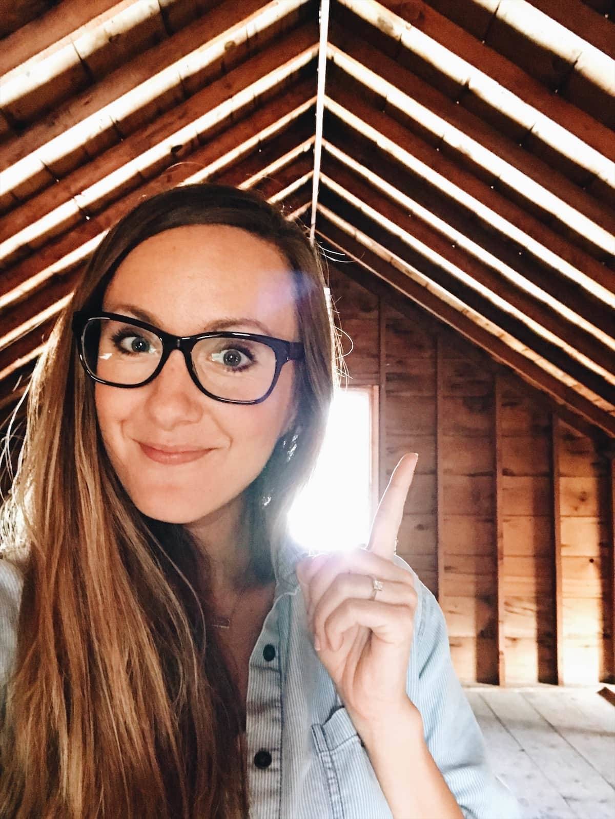 A young woman wearing large eyeglasses points to an arched ceiling with exposed wood.