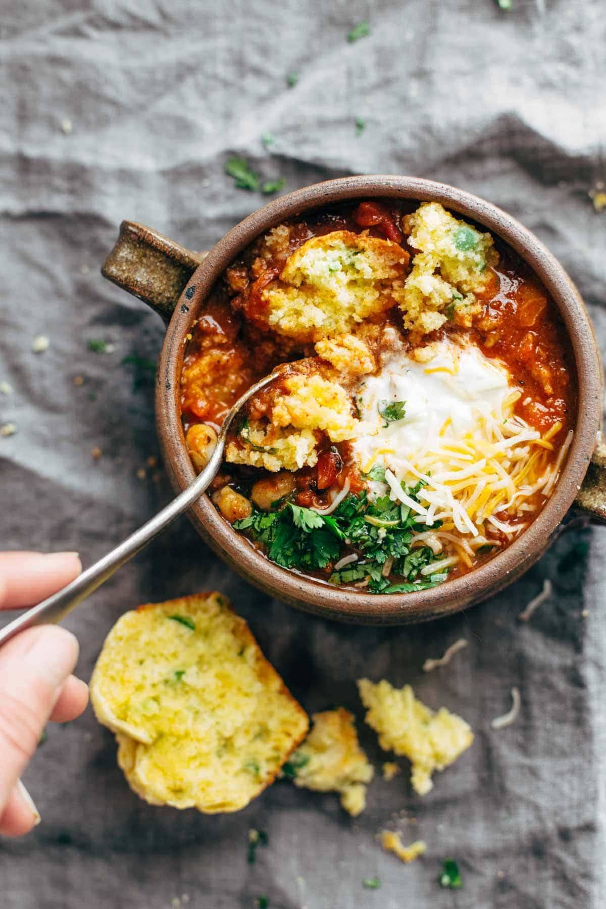 Spicy Posole in a bowl with a spoon and Cheesy Jalapeño Cornbread Muffins. 