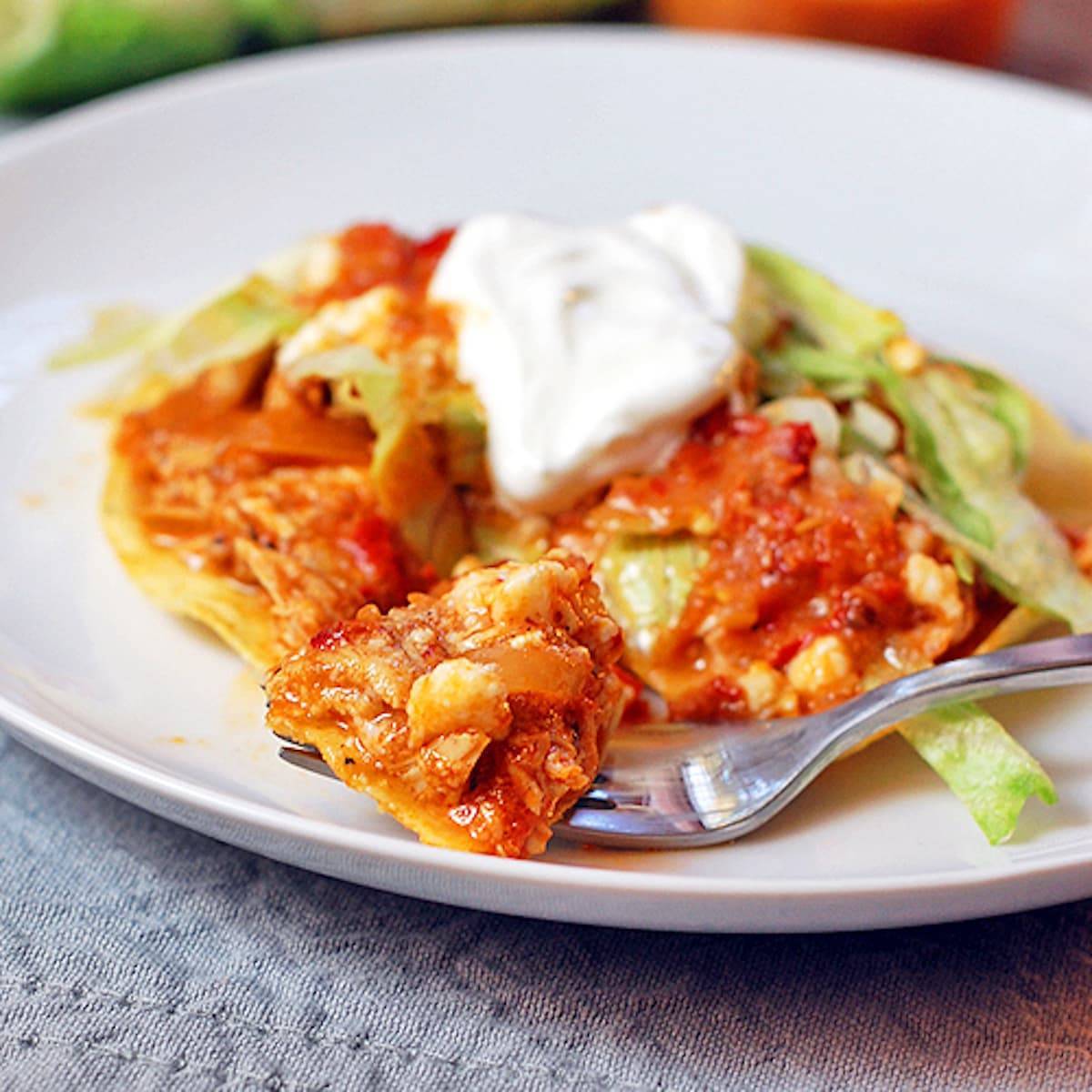 Spicy chicken tostadas on a white plate with sour cream topping.