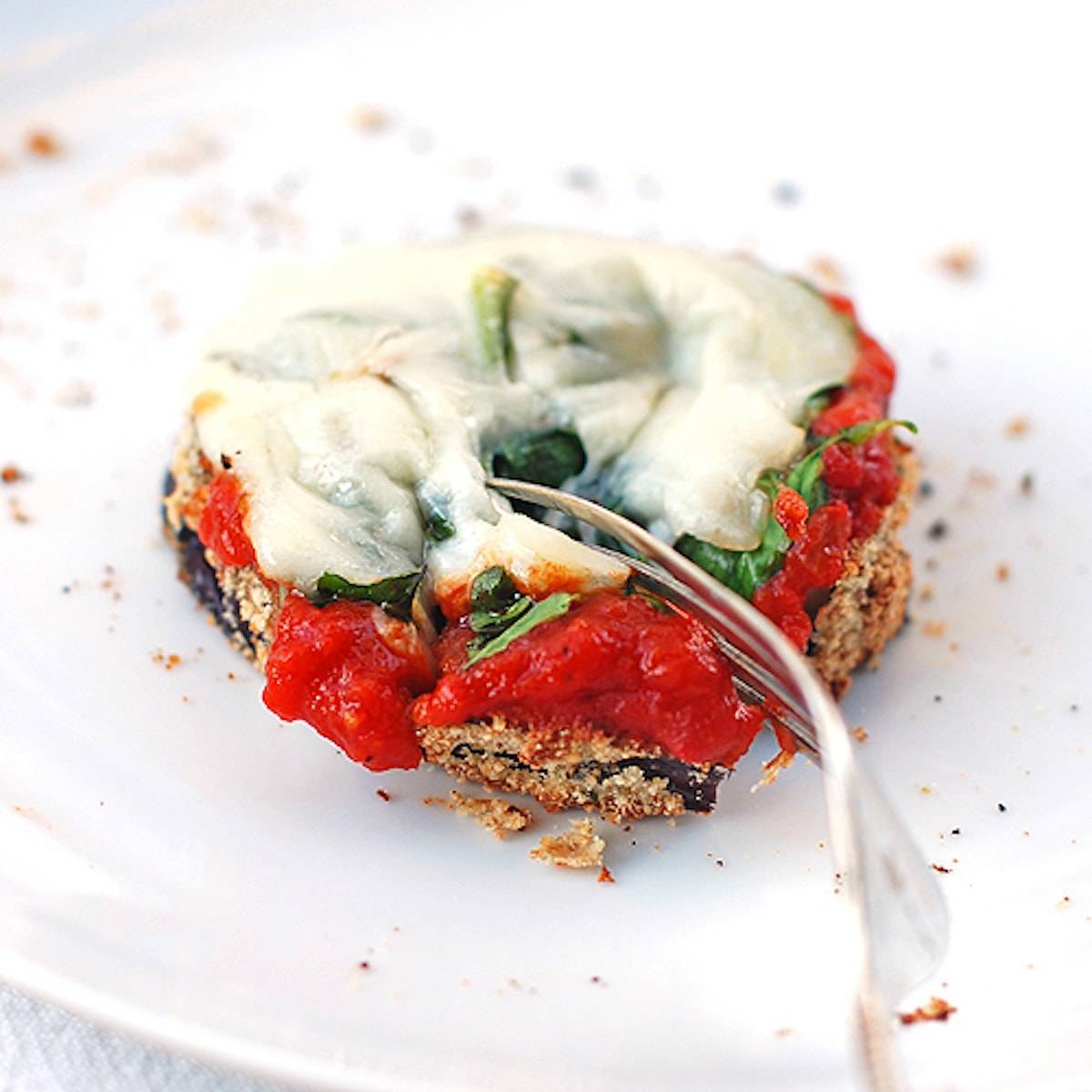Eggplant pizza topped with marinara and melted cheese on a plate with a fork.