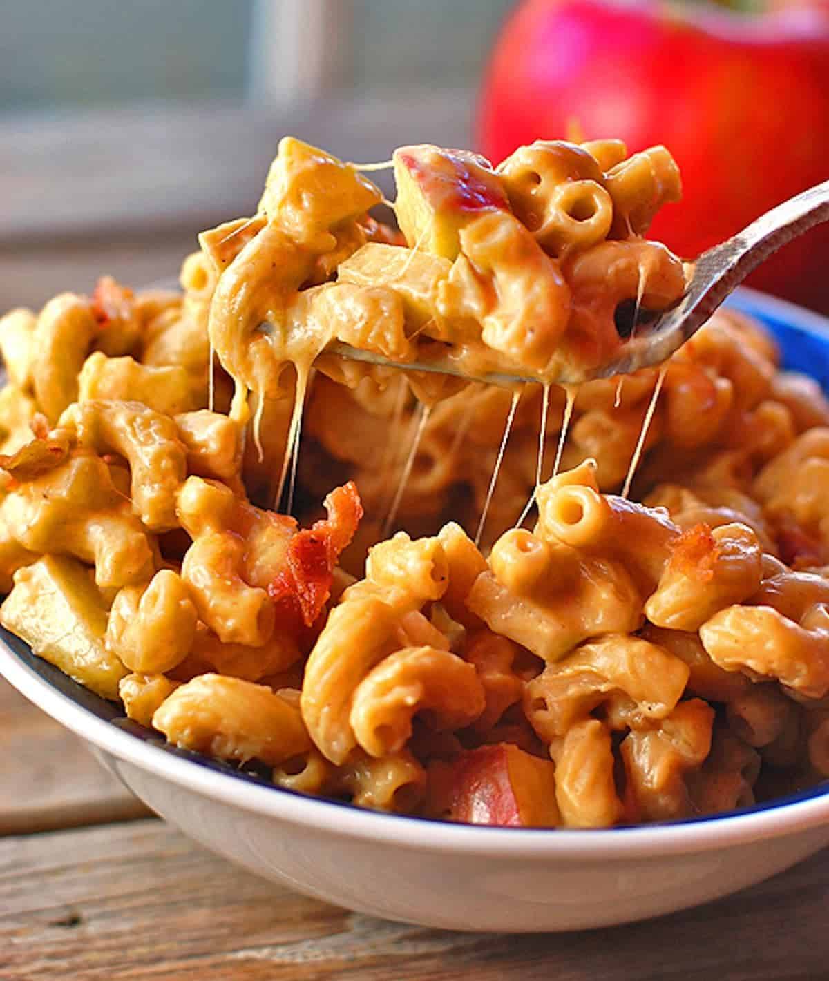 Butternut squash mac and cheese with caramelized onions, crispy bacon, and fresh sweet apples on a fork.